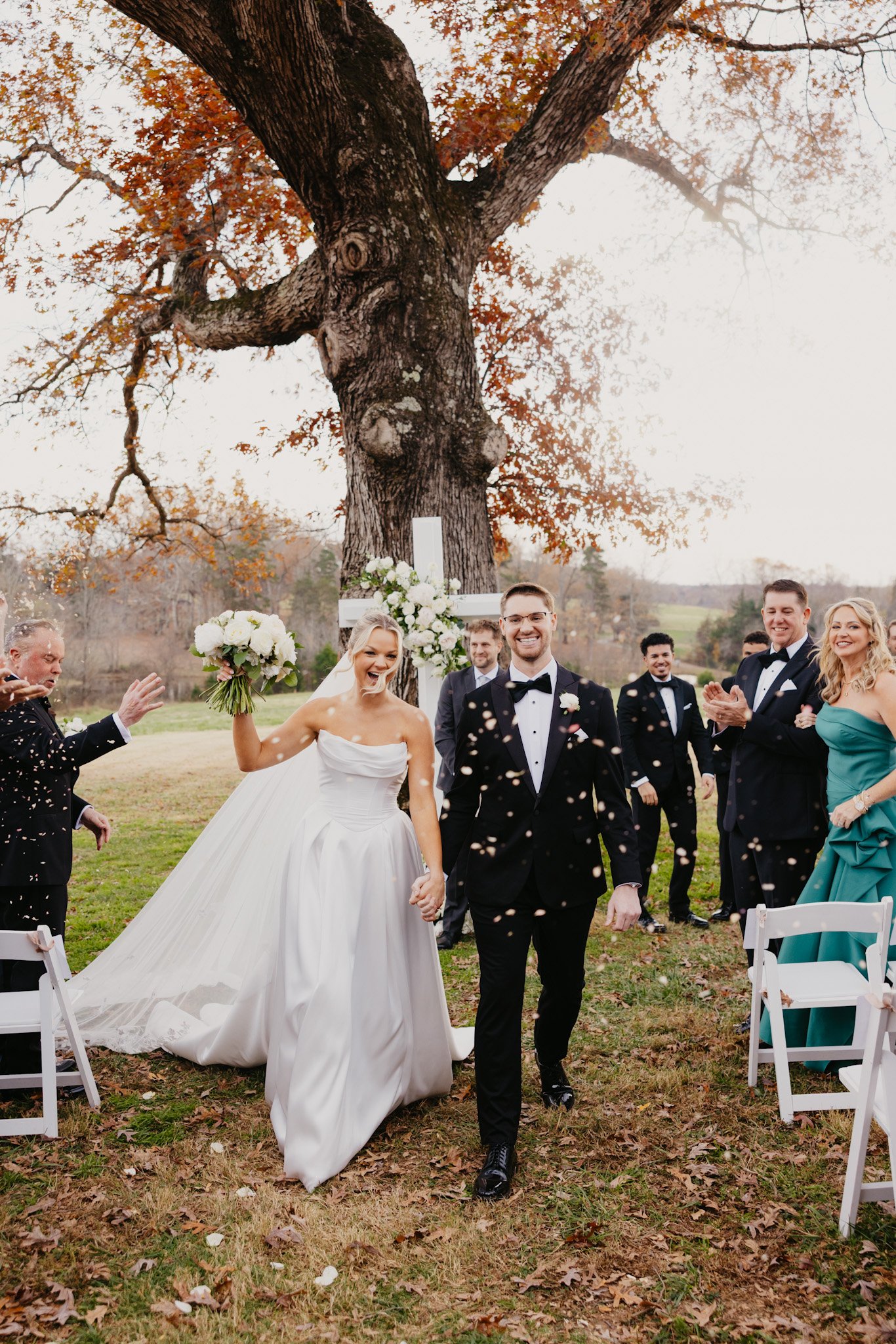 A bride and groom walking through falling confetti as guests applaud at an outdoor ceremony
